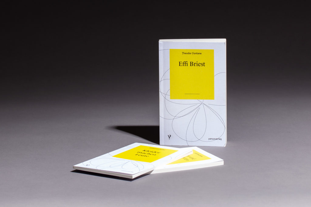 Yanus Verlag Bücher stehend und liegend auf grauem Hintergrund